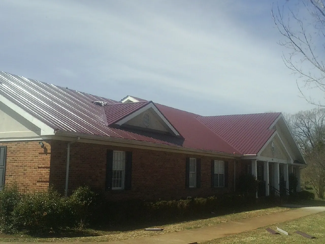Red metal roof with gabled entries on a long brick building, from a Hail Damage Roof Repair job in Bethpage