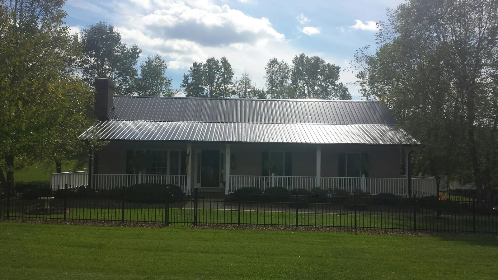 Gray metal roof on a brick ranch with a full width front porch — Gutter Guard Installation work by our crew in Bethpage