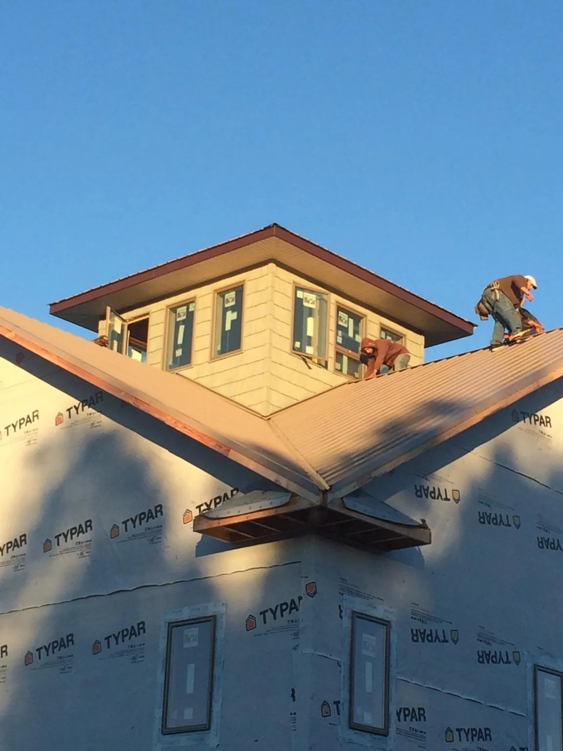 Roofers working around a rooftop cupola on a new metal roof at sunset — Roof Waterproofing in Bethpage by Roofing Brothers